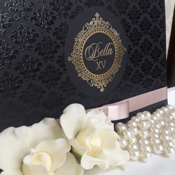 Que Encanta à Primeira Vista A celebração dos 15 anos é um dos momentos mais marcantes na vida de uma jovem. Conhecida como a festa de debutante, essa ocasião representa a transição da infância para a juventude e merece ser anunciada com todo o charme, sofisticação e personalidade. E tudo começa com o convite. Mais do que apenas um informativo sobre data e local, o convite de 15 anos é o primeiro contato dos convidados com o estilo e a essência da festa. Por isso, convidar com elegância é essencial. Neste post, vamos apresentar uma verdadeira obra de arte: um modelo de convite debutante que une delicadeza, exclusividade e sofisticação. Ele foi pensado para encantar desde o primeiro olhar e ficar guardado como lembrança desse dia tão especial. Se você está buscando inspiração para criar um convite inesquecível, continue lendo e descubra cada detalhe desta peça única. O Encanto Começa pelo Exterior O primeiro impacto do convite de 15 anos acontece no momento em que ele é entregue. Este modelo é confeccionado em um papel rosa brilhante de alta gramatura, que oferece uma textura luxuosa e um brilho sutil que reflete a luz com suavidade. O tom de rosa escolhido remete à feminilidade e à doçura dessa fase da vida, enquanto o brilho acrescenta um toque de glamour e celebração. Para selar o convite com ainda mais requinte, utilizamos um delicado lacre de cera em tom rosé, que carrega o símbolo de um brasão personalizado com as iniciais da debutante. O lacre é decorado com uma pequena flor sempre-viva, que adiciona um toque artesanal e romântico, remetendo à ideia de eternidade – afinal, os momentos especiais devem ser eternizados. A Magia Continua por Dentro Ao abrir o convite, o encantamento só aumenta. O conteúdo interno é impresso em papel Aspen, conhecido por sua leveza, textura acetinada e excelente qualidade de impressão. O design foi cuidadosamente desenvolvido para refletir a personalidade da debutante e o estilo da festa. O layout conta com uma composição de flores silvestres em aquarela, distribuídas de forma harmônica nas bordas, trazendo a sensação de um jardim delicado e natural. Essas flores não apenas embelezam o convite, mas também transmitem frescor, leveza e a alegria típica dos 15 anos. O centro do convite é reservado para o texto principal, onde as informações da festa são dispostas de forma clara e elegante. O grande destaque é o nome da debutante, que aparece em hot stamp rosé, uma técnica que aplica uma camada metálica brilhante em alto relevo, criando um efeito visual sofisticado e memorável. Este detalhe atrai o olhar imediatamente, valorizando ainda mais o nome da aniversariante e demonstrando a importância da ocasião. O brasão que aparece no lacre é repetido discretamente no topo do convite, integrando o design com consistência e refinamento. Ele simboliza a nobreza e a tradição da cerimônia de debutante, ao mesmo tempo que imprime um ar moderno e exclusivo. Convidando com Elegância e Personalidade Esse modelo de convite debutante foi criado para quem deseja convidar com elegância, expressando carinho e cuidado com cada convidado. A escolha dos materiais, as técnicas de impressão e os elementos decorativos foram pensados para transmitir sofisticação e personalidade, revelando um pouco do que os convidados podem esperar da celebração. Afinal, o convite de 15 anos não é apenas um pedaço de papel: ele é o cartão de visitas da festa, o primeiro capítulo de uma história inesquecível. Ele antecipa emoções, desperta expectativas e faz cada pessoa se sentir especial e desejada para compartilhar esse momento tão único. Se você está planejando uma festa de 15 anos e quer impressionar desde o primeiro detalhe, inspire-se neste modelo de convite e transforme o anúncio da sua celebração em uma verdadeira experiência. Aposte em materiais nobres, toques personalizados e, acima de tudo, convidando com elegância. Porque os 15 anos passam, mas a memória de um convite bem feito dura para sempre.